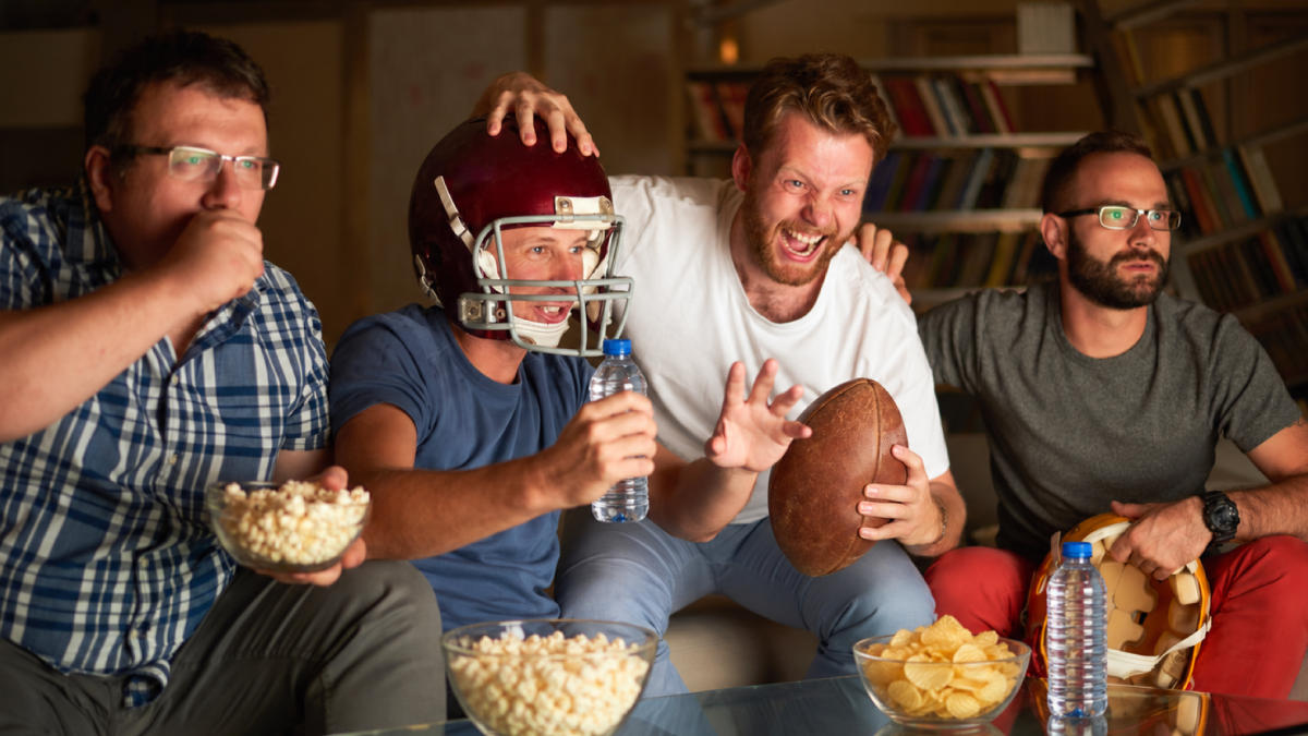 Four football fans cheer while watching a game together at home.